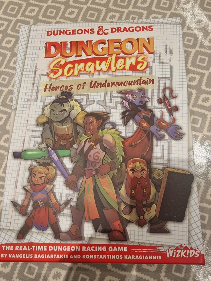 Cover of the board game "Dungeon Crawlers: Heroes of Undermountain," featuring colorful illustrations of diverse fantasy characters, including an orc, elf, and dwarf, set against a graph paper background. The title emphasizes the game's real-time dungeon racing theme, created by Vangelis Bagiartakis and Konstantinos Karagiannis, published by WizKids.