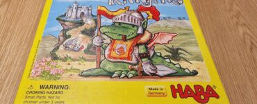 Colorful board game box for "Knuckling Knights" by HABA, featuring a cartoon dragon in knight armor, set against a whimsical castle backdrop. The box includes a warning label about choking hazards for small parts. Made in Germany.