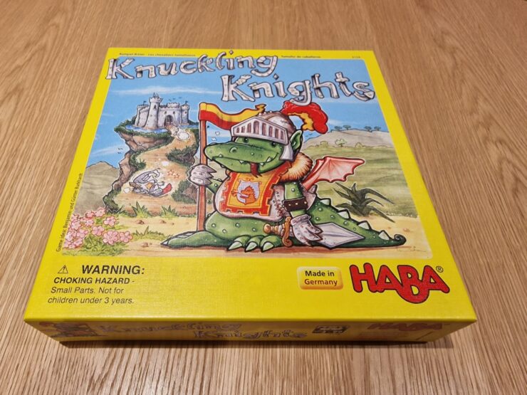 Colorful board game box for "Knuckling Knights" by HABA, featuring a cartoon dragon in knight armor, set against a whimsical castle backdrop. The box includes a warning label about choking hazards for small parts. Made in Germany.