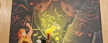 Box cover of Kingdomino Origins board game featuring vibrant artwork of two cave people, one holding a torch, set against a prehistoric backdrop. The game is designed for 2-4 players, ages 8 and up, with a playtime of approximately 25 minutes. Published by Blue Orange Games, created by Bruno Cathala and Cyril Bouquet.