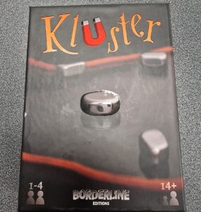 Box of the game "KluSter" by Borderline Editions, featuring a metallic game piece on a dark background, suitable for 1-4 players aged 14 and up.