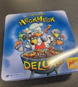 Board game box for "Heckmeck Deluxe" by Reiner Knizia, featuring cartoonish chickens and a chef grilling skewers, with vibrant colors and a playful design. Ideal for family game nights and gatherings.
