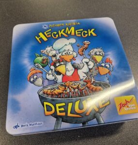Board game box for "Heckmeck Deluxe" by Reiner Knizia, featuring cartoonish chickens and a chef grilling skewers, with vibrant colors and a playful design. Ideal for family game nights and gatherings.