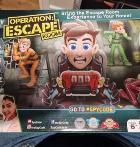 Colorful board game box for "Operation: Escape Room" featuring characters engaged in various escape activities. The design includes instructions to "Search, Solve, Escape" and highlights the game's social aspect for 2-6 players, ages 6 and up. The packaging also features social media handles and showcases awards, emphasizing the fun and interactive escape room experience at home.