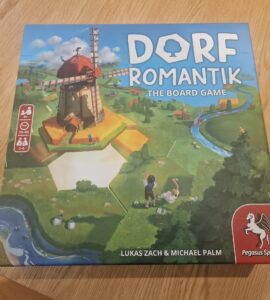 Box of Dorf Romantik: The Board Game featuring a colorful illustration of a windmill and a scenic landscape. Designed for 1-6 players aged 8 and up, with gameplay lasting 30-60 minutes. Created by Lukas Zach and Michael Palm, published by Pegasus Spiele.