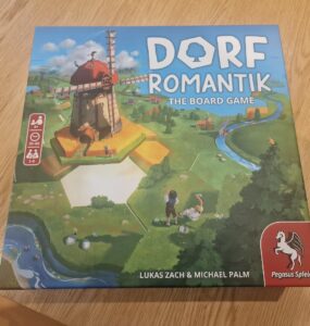 Box of Dorf Romantik: The Board Game featuring a colorful illustration of a windmill and a scenic landscape. Designed for 1-6 players aged 8 and up, with gameplay lasting 30-60 minutes. Created by Lukas Zach and Michael Palm, published by Pegasus Spiele.