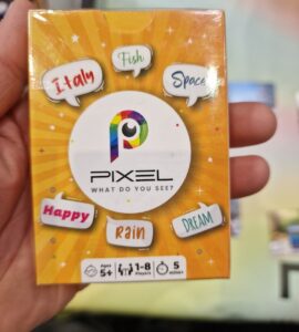 Image of the board game "Pixel," featuring a colorful box design with the title prominently displayed. The box includes playful words like "Italy," "Fish," "Space," "Happy," "Rain," and "Dream," indicating the game's creative theme. It is suitable for ages 5 and up, accommodating 1-8 players, and designed for quick play sessions of 5 minutes or more.