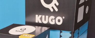 Kugo game boxes displayed against a blue and black background, featuring the words "PLAY," "TRIX," and "BUILD," showcasing the interactive and creative nature of the game.
