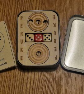Peruke board game set displayed on a wooden surface, featuring a wooden game board with dice, a rules booklet, and a metal tin. Ideal for family game nights and strategic play, emphasizing handcrafted quality from the UK.