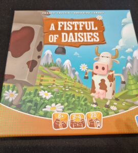 Board game "A Fistful of Daisies" featuring a cartoon cow on the cover, designed for 2-4 players aged 6 and up, with a playtime of approximately 20 minutes. The vibrant illustration includes a pastoral landscape with flowers and mountains, emphasizing a fun, family-friendly theme.