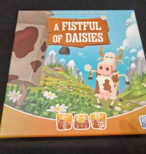 Board game "A Fistful of Daisies" featuring a cartoon cow on the cover, designed for 2-4 players aged 6 and up, with a playtime of approximately 20 minutes. The vibrant illustration includes a pastoral landscape with flowers and mountains, emphasizing a fun, family-friendly theme.