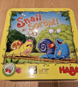Colorful game box for "Snail Sprint!" by HABA, featuring cartoon snails racing in a vibrant outdoor setting. The box highlights the game's magnetic snail racer feature and is designed for 2-4 players aged 2 and up.