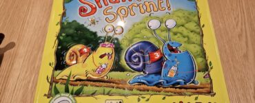 Colorful game box for "Snail Sprint!" by HABA, featuring cartoon snails racing in a vibrant outdoor setting. The box highlights the game's magnetic snail racer feature and is designed for 2-4 players aged 2 and up.
