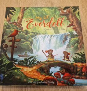 Cover of the board game "My Lil' Everdell," featuring vibrant artwork by Andrew Bosley. The illustration showcases a whimsical forest scene with characters like mice and frogs, a waterfall, and lush greenery, highlighting the enchanting world of Everdell. Perfect for family game nights and young players.