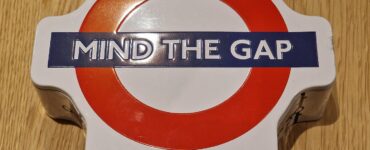 Mind the Gap card game in a round tin box with a red and white London Underground logo, resting on a wooden surface.