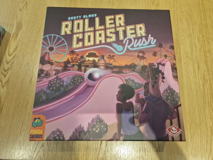 Board game box for "Roller Coaster Rush" by Scott Almes, featuring vibrant artwork of a theme park with roller coasters and attractions. The design includes playful characters enjoying the amusement park atmosphere, highlighting the game's fun and engaging theme. Published by Pandasaurus Games.