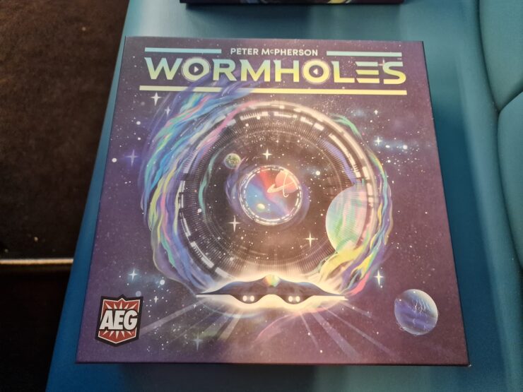 Colorful board game box for "Wormholes" by Peter McPherson, featuring a cosmic design with swirling galaxies and planets, highlighting its space-themed gameplay.