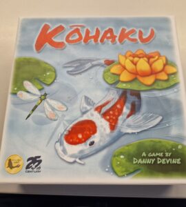 Colorful board game box for "Kōhaku" designed by Danny Devine, featuring a koi fish, a water lily, and dragonflies, highlighting its serene aquatic theme.