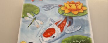 Colorful board game box for "Kōhaku" designed by Danny Devine, featuring a koi fish, a water lily, and dragonflies, highlighting its serene aquatic theme.