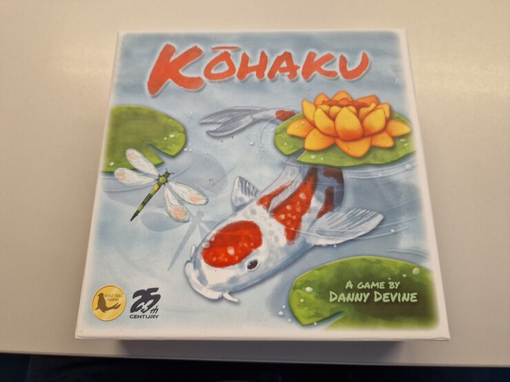 Colorful board game box for "Kōhaku" designed by Danny Devine, featuring a koi fish, a water lily, and dragonflies, highlighting its serene aquatic theme.