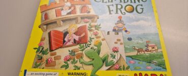 Colorful box of the board game "Castle Climbing Frog" by HABA, featuring playful illustrations of a frog, castle, and characters. The bright yellow packaging highlights the game’s focus on skill and memory, with a warning label for small parts. Made in Germany.