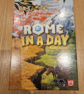 Board game "Rome in a Day" featuring vibrant artwork of ancient Rome, with the tagline "Veni, Vidi, Divisi," designed by Evgeny Petrov, published by Red Cat Games. The cover showcases a picturesque landscape with buildings, greenery, and a horse, set against a backdrop of the iconic Colosseum.