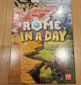 Board game "Rome in a Day" featuring vibrant artwork of ancient Rome, with the tagline "Veni, Vidi, Divisi," designed by Evgeny Petrov, published by Red Cat Games. The cover showcases a picturesque landscape with buildings, greenery, and a horse, set against a backdrop of the iconic Colosseum.