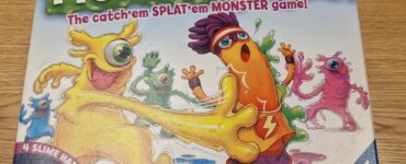 Colorful board game box for "Monster Splat" by Ravensburger, featuring playful cartoon monsters and the tagline "The catch'em SPLAT'em MONSTER game!" Includes details about the game suitable for ages 5 to 99 and highlights the inclusion of four slime hands.