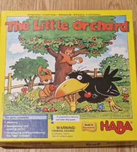 Colorful box of "The Little Orchard" board game by HABA, featuring playful illustrations of a crow, a squirrel, and a tree with fruit. The box promotes memory skills, color recognition, and cooperative play for young children. Made in Germany.