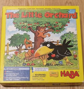 Colorful box of "The Little Orchard" board game by HABA, featuring playful illustrations of a crow, a squirrel, and a tree with fruit. The box promotes memory skills, color recognition, and cooperative play for young children. Made in Germany.