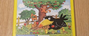 Colorful box of "The Little Orchard" board game by HABA, featuring playful illustrations of a crow, a squirrel, and a tree with fruit. The box promotes memory skills, color recognition, and cooperative play for young children. Made in Germany.