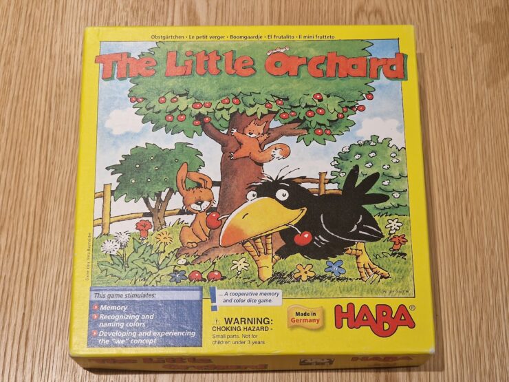 Colorful box of "The Little Orchard" board game by HABA, featuring playful illustrations of a crow, a squirrel, and a tree with fruit. The box promotes memory skills, color recognition, and cooperative play for young children. Made in Germany.