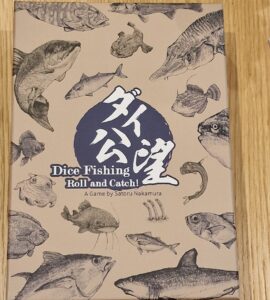Dice Fishing game box featuring various fish illustrations, titled "Dice Fishing: Roll and Catch!" designed by Satoru Nakamura, set against a light brown background.