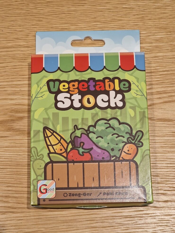 Colorful packaging of vegetable stock featuring cartoon vegetables like corn, tomatoes, and broccoli, on a wooden table. The product is branded as "Vegetable Stock" and is associated with a game called "Zong-Ger."