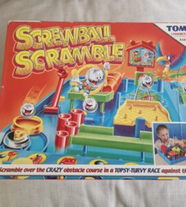 Colorful box of the game "Screwball Scramble" by TOMY featuring a crazy obstacle course for one or more players. Suitable for ages 5 and up, the game challenges players to navigate balls through various obstacles in a timed race. The box shows children engaged in gameplay, highlighting the fun and competitive nature of the game.