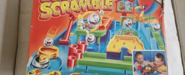 Colorful box of the game "Screwball Scramble" by TOMY featuring a crazy obstacle course for one or more players. Suitable for ages 5 and up, the game challenges players to navigate balls through various obstacles in a timed race. The box shows children engaged in gameplay, highlighting the fun and competitive nature of the game.