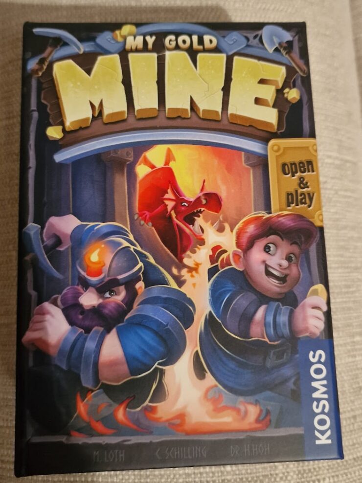 Board game box for "My Gold Mine," featuring two miners in action, one with a pickaxe and the other holding a gold coin, with a dragon in the background. The vibrant artwork showcases a fantasy theme, emphasizing adventure and treasure hunting.