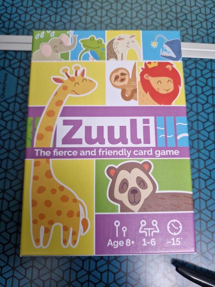 Colorful box of the card game "Zuuli," featuring playful animal illustrations including a giraffe, sloth, lion, and more. The design highlights that the game is suitable for ages 8 and up, supports 1 to 6 players, and has a playtime of approximately 15 minutes.