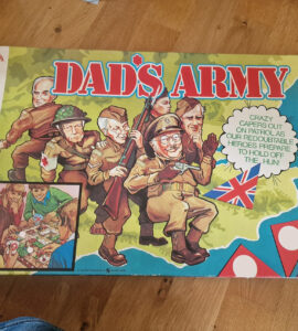 Box cover of the board game "Dad's Army," featuring colorful illustrations of characters in military attire, including a soldier with a rifle and others in various poses. The design includes the British flag and playful text, highlighting the game's theme of humor and strategy. Ideal for fans of classic British television and board games.