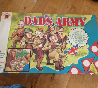 Box cover of the board game "Dad's Army," featuring colorful illustrations of characters in military attire, including a soldier with a rifle and others in various poses. The design includes the British flag and playful text, highlighting the game's theme of humor and strategy. Ideal for fans of classic British television and board games.