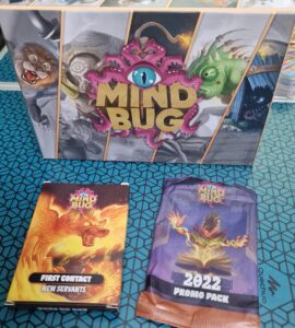 Box set of the card game "Mind Bug" featuring the main game box, a "First Contact" expansion pack, and a "2022 Promo Pack." The game combines strategy and fantasy elements, showcasing vibrant artwork of various characters and creatures.