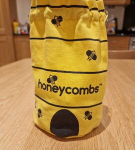 Yellow fabric bag featuring a bee design and the word "honeycombs," placed on a wooden table in a kitchen setting.