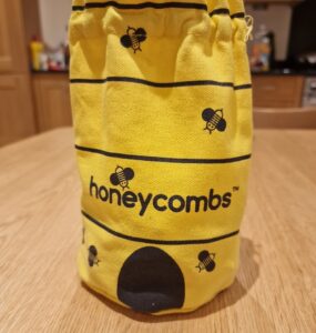 Yellow fabric bag featuring a bee design and the word "honeycombs," placed on a wooden table in a kitchen setting.