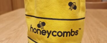 Yellow fabric bag featuring a bee design and the word "honeycombs," placed on a wooden table in a kitchen setting.