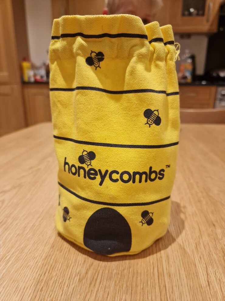 Yellow fabric bag featuring a bee design and the word "honeycombs," placed on a wooden table in a kitchen setting.