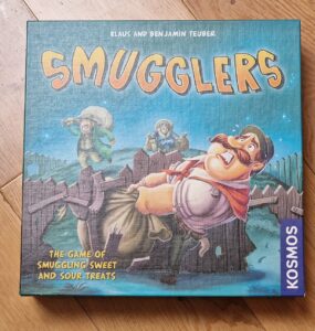 Board game box for "Smugglers," featuring colorful artwork and characters involved in the game of smuggling sweets and sour treats. Published by Kosmos, designed by Klaus and Benjamin Teuber.