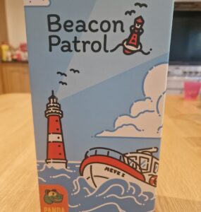 Box design of the board game "Beacon Patrol" by Torben Ratzlaff, featuring a colorful illustration of a lighthouse, a boat named "Meves 2," and playful clouds. The box is branded with the Panda Saurus Games logo, set against a light blue background.