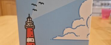 Box design of the board game "Beacon Patrol" by Torben Ratzlaff, featuring a colorful illustration of a lighthouse, a boat named "Meves 2," and playful clouds. The box is branded with the Panda Saurus Games logo, set against a light blue background.