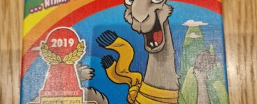 Colorful board game box for L.A.M.A. by Reiner Knizia, featuring a cartoon llama and a rainbow background. The box highlights the game's age recommendation of 8+, its nomination for the Spiel des Jahres award in 2019, and the logo of Amigo Spiele.