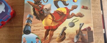 Colorful game box for Buckaroo!, a saddle-stacking game featuring a playful mule, suitable for ages 4 and up, designed for 2-4 players. The packaging displays various game pieces and includes a warning about small parts. Hasbro Gaming branding is visible.